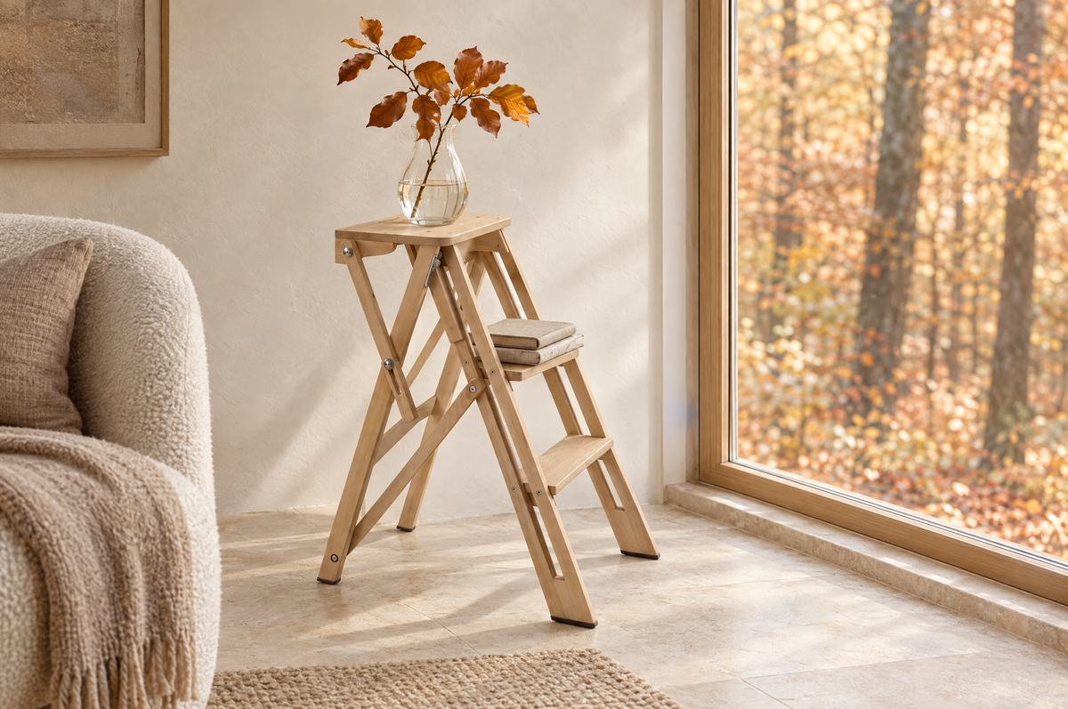 Escalera pequeña de madera de haya usada como mesita junto a una ventana con vistas a un hayedo en otoño